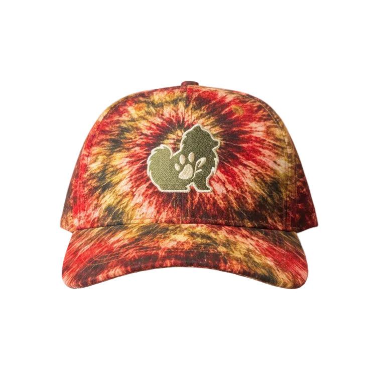 A close-up of a curved-brim cap with a red, orange, and yellow tie-dye pattern and a central green paw-print logo, resting against an olive green fuzzy fabric background.