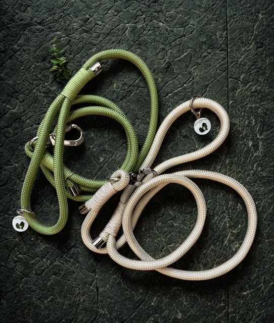 Two dog leashes, one green and one khaki, on a dark textured surface.