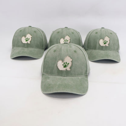 Four sage green baseball caps arranged on a white background, each featuring an embroidered white silhouette of a small dog with a green paw print on the front.
