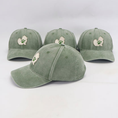 Four sage green baseball caps with a small white embroidered dog patch and green paw print on the front, displayed on a light gray background.