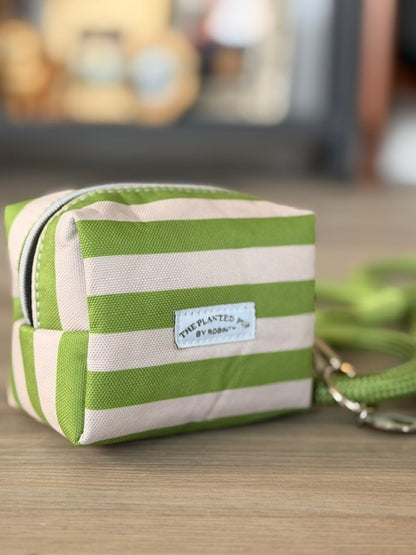 A small zippered pouch with horizontal lime green and cream stripes, featuring a white fabric label that reads 'THE PLANTED POT by KASU'.