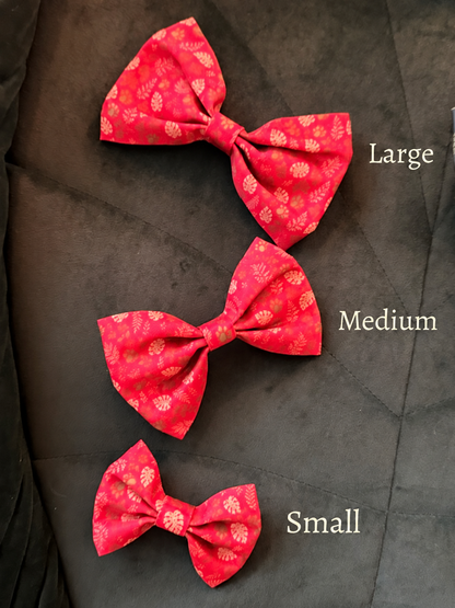 Three red fabric bow ties with a small white floral pattern are displayed on a dark gray quilted surface, labeled Large, Medium, and Small.